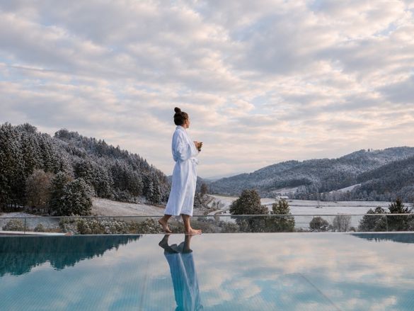 Frau steht am Infinity Pool im Adults Only Bereich und genießt die Aussicht auf die winterliche Landschaft
